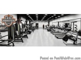 The image shows a large gym with a variety of exercise equipment. The floor is made of concrete and the walls are painted whi...