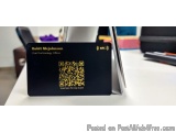 The image shows a black business card with a QR code on it. The card is placed on a desk with a laptop and other office suppl...