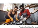The image shows two young men in a kitchen, both wearing overalls and hard hats. They are kneeling on the floor and appear to...