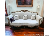 The image shows a white sofa in a room with wooden flooring. The sofa has an ornate, carved design with a curved backrest and...