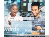 The image shows a man and a woman sitting at a desk with a laptop in front of them. They are both smiling and appear to be en...