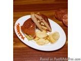 The image shows a plate with a sandwich and a side of potato chips. The sandwich is made with two slices of toasted bread, fi...