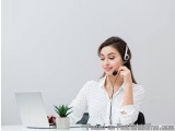 The image shows a young woman sitting at a desk with a laptop and a small plant in front of her. She is wearing a white blous...