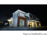 The image shows a modern two-story house at night. The house is lit up with a warm glow, creating a cozy and inviting atmosph...