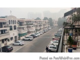 The image shows a street view of a residential area with a row of buildings on both sides. The buildings are white with balco...