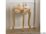 The image shows a gold-colored console table in a corner of a room. The table has a round top with a decorative design on the...