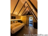The image shows a bedroom with a high ceiling made of wooden beams. The walls are painted in a light yellow color and there i...