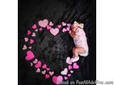 The image shows a baby girl sleeping peacefully on a black background. She is wearing a pink onesie and a white headband with...