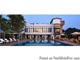 The image shows a modern luxury villa with a large swimming pool in the center. The villa has a white exterior with large win...
