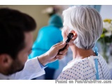 The image shows a doctor examining an elderly woman's ear with an otoscope. The doctor is wearing a white coat and is holding...
