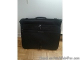The image shows a black suitcase lying on a wooden floor. The suitcase appears to be made of a hard material and has a handle...