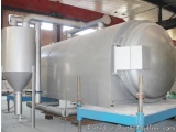 The image shows a large industrial machine inside a warehouse. The machine is made of stainless steel and has a cylindrical s...
