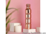 The image shows a tall, cylindrical water bottle with a copper-colored body and a copper cap. The bottle is placed on a white...