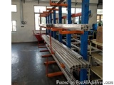 The image shows a large warehouse with a long row of blue and orange metal racks. The racks are arranged in a neat and orderl...