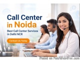 The image shows a group of people working in a call center in Noida, India. The people are wearing headsets and are sitting a...