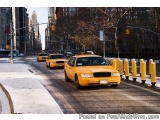 The image shows a busy street in New York City. There are several yellow taxi cabs parked on the side of the road. The street...