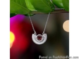 The image is a close-up of a necklace hanging from a branch with green leaves. The necklace is made of silver and has a penda...