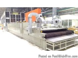 The image shows a large industrial machine in a factory. The machine is made of stainless steel and has a long, rectangular s...