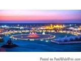 The image is an aerial view of a city at night. The sky is a beautiful pink and purple color, with the sun setting in the bac...