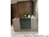 The image shows a modern reception desk in a room with a wooden wall in the background. The desk is made of light-colored woo...