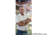 The image is a portrait of a middle-aged man standing in a shopping mall. He is wearing a white polka-dot shirt with blue jea...