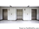 The image shows three elevators in a modern building. The elevators are made of stainless steel and have a sleek, metallic fi...