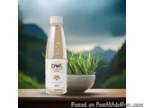 The image shows a bottle of DWA Skin Radiant Water on a wooden table. The bottle is transparent and has a white cap. The labe...