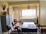 The image shows a small room with a single bed in the center. The bed has a white comforter and two pillows. There is a windo...