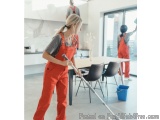 The image shows a young woman wearing orange overalls and a gray t-shirt, cleaning the floor with a mop. She is standing in a...