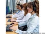 The image shows a group of four people working in a call center. They are all wearing white shirts and are sitting at desks w...