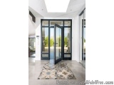 The image shows the entrance of a modern house with a large glass door. The door is made of black glass and has a handle on t...