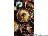 The image shows a collection of Indian food items arranged on a wooden table. There are six bowls of different types of food,...