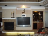 The image shows a living room with a fireplace and a flat-screen TV mounted on the wall above it. The fireplace has a mantelp...