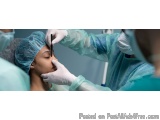 The image shows a close-up of a surgeon performing an operation on a patient. The surgeon is wearing a blue surgical gown, a...