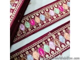 The image shows a close-up of a piece of fabric with a decorative border. The fabric appears to be made of a dark red materia...