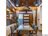 The image shows a modern and luxurious dining area in a home. The room has a wooden ceiling with a ceiling fan and recessed l...