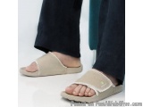 The image shows a pair of feet wearing beige sandals. The sandals have a flat sole and a strap across the top of the foot wit...