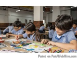 The image shows a group of children sitting at a table in a classroom. They are all wearing blue school uniforms and are enga...