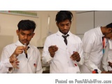 The image shows three young men in white lab coats standing in a laboratory. They are holding test tubes and appear to be con...