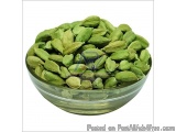The image shows a glass bowl filled with green cardamom pods. The bowl is round and has a clear glass rim. The pods are small...