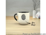 The image shows a white ceramic mug with a black handle on a wooden table. On the mug, there is a black fingerprint design in...