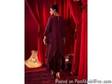 The image shows a woman standing in front of a red curtain. She is wearing a long, flowing purple dress with a high neckline...