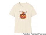 The image is of a light beige t-shirt with a graphic design on the front. The design features a cartoon pumpkin with a witch...