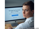 The image shows a young woman sitting in front of a computer monitor. She is wearing a white collared shirt and has short blo...
