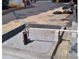 The image shows a concrete structure with a small pump attached to it. The structure appears to be a water well or a drainage...
