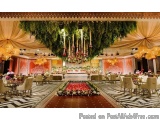 The image shows an elegant and luxurious wedding reception hall. The hall is decorated with a large floral arch hanging from...