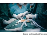 The image shows a group of surgeons performing an operation in an operating room. The surgeons are wearing green surgical gow...
