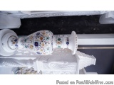 The image shows a white vase with intricate floral designs on it. The vase is sitting on a white pedestal with a decorative b...