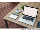 The image shows a wooden table with a laptop on it. The laptop is open and has a blank screen. Next to the laptop, there is a...