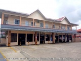 The image shows a two-story building with a beige exterior and a red roof. The building has a balcony on the second floor wit...
